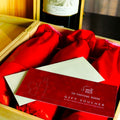 A gift voucher from The Wine Rack Tasting Room placed on a red surface inside a wooden box, with wine bottles in the background.